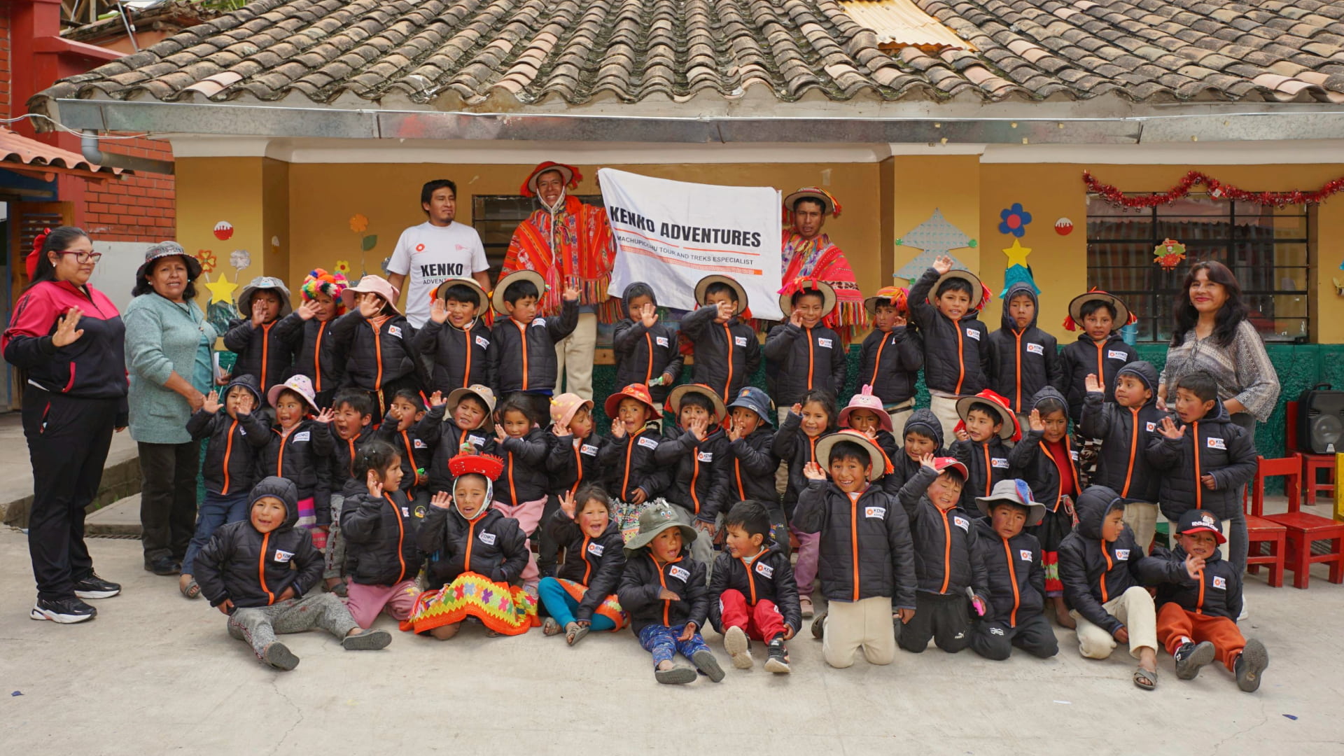 A joyful group of children after a hot chocolate gathering by Kenko Adventures, proudly wearing jackets they received, with the Kenko Adventures banner visible, embodying solidarity and festive cheer.